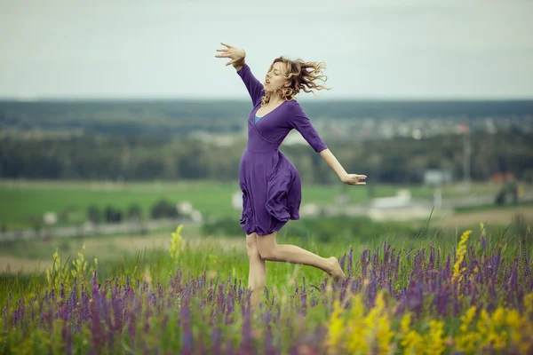 Молода дівчина в вінтажній сукні, що йде через поле квітів мудреця . — стокове фото