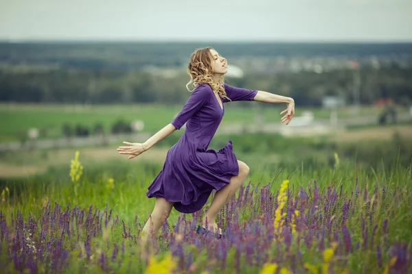 Молода дівчина в вінтажній сукні, що йде через поле квітів мудреця . — стокове фото