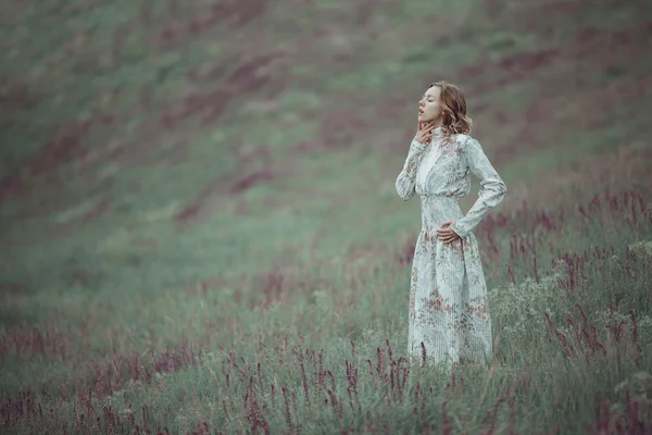 Jeune fille en robe vintage marchant à travers le champ de fleurs de sauge . — Photo