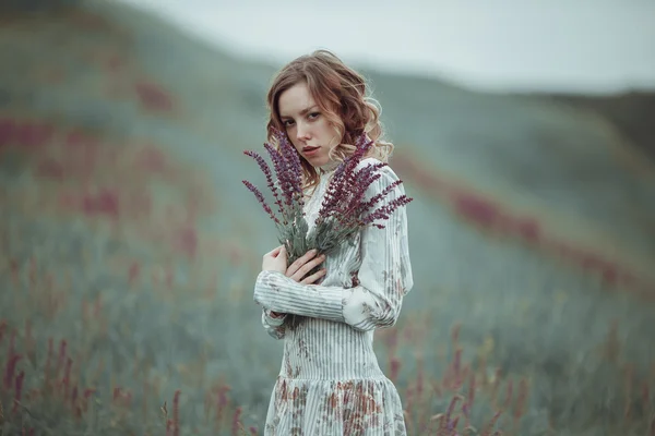 Junges Mädchen im Vintage-Kleid geht durch Salbeiblumenfeld. — Stockfoto