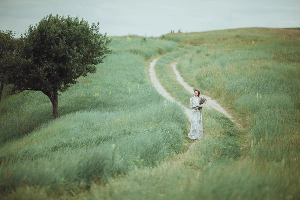 Junges Mädchen im Vintage-Kleid geht durch Salbeiblumenfeld. — Stockfoto