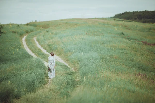 Jeune fille en robe vintage marchant à travers le champ de fleurs de sauge . — Photo