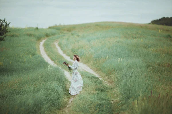 Chica joven en vestido vintage caminando por el campo de flores de salvia . — Foto de Stock