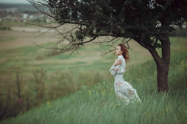 Chica joven en vestido vintage de pie cerca del árbol solitario — Foto de Stock
