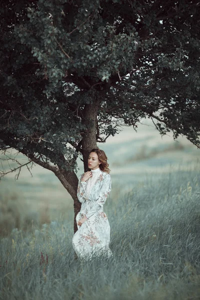 Giovane ragazza in abito vintage in piedi vicino albero solitario — Foto Stock