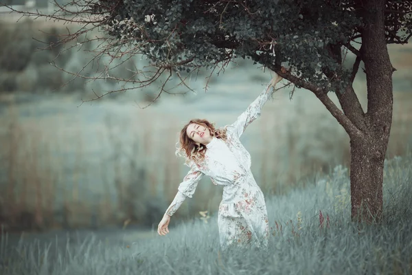 Chica joven en vestido vintage de pie cerca del árbol solitario — Foto de Stock