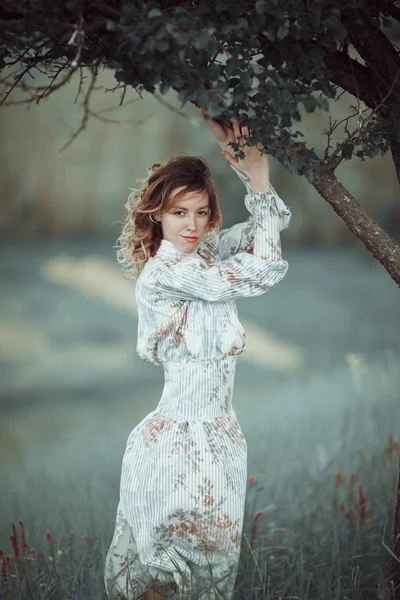 Ung flicka i vintage klänning står nära ensamt träd — Stockfoto