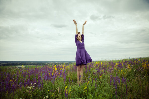 Young girl in vintage dress walking through sage flower field.