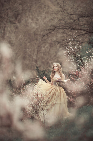 Princess looking girl walks in spring garden near blooming trees