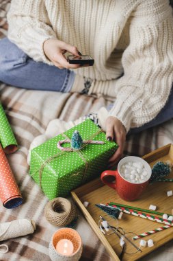 Akıllı telefonlu bir kadın sosyal ağlar için yılbaşı resmi ya da Noel resmi çekiyor. İçerik yaratılıyor. Tahta tepside kakao kupası şekerlemeler, oyuncak ağaç, mum, yıldızlar, paketlenmiş hediye..