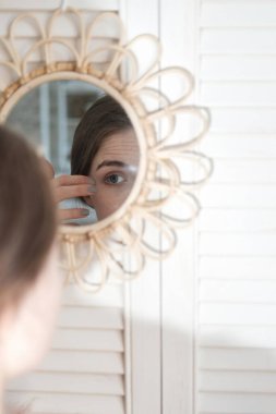 Banyodaki genç ve güzel kadın aynadaki yansımasını inceliyor. Kadın sabah teni ve saç bakımı prosedürleri..