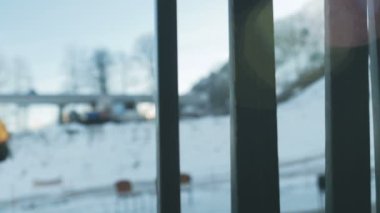 Kürk kulaklıklı, güneş gözlüklü, turkuaz ceketli, eşarplı ve sırt çantalı genç bir kadın güneşin ve havanın tadını çıkarıyor. Kayak merkezinin etrafında, kar, dağlar, asansörler. Yavaş çekim.