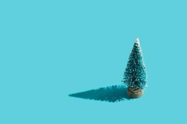 Minimum mavi arka planda sert gölgeli oyuncak plastik Noel ağacı. Noel ve Yeni Yıl arkaplanı, gelecek tatiller için tebrik ederim. Düz yatıyordu. Üst Manzara. Metin için yer.