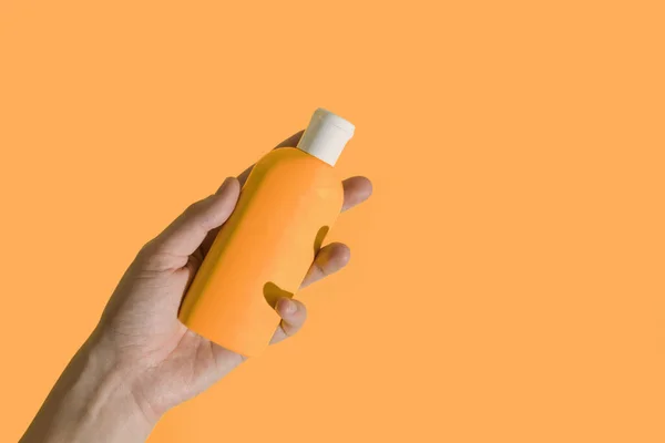 A mão feminina segura uma garrafa de creme em um fundo amarelo brilhante de calêndula. Cor da moda do ano 2021. — Fotografia de Stock