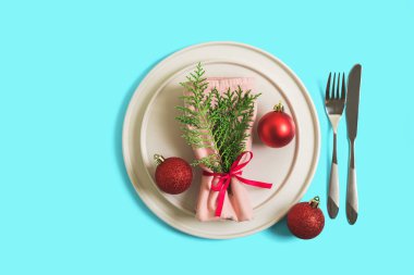 Noel ve Yeni Yıl kutlamaları için tabak ve çatal bıçakla servis edildi. Tabakta Noel ağacı dallı bir peçete var, kırmızı toplar. Parlak mavi arka planda düz çizgi. Üst görünüm