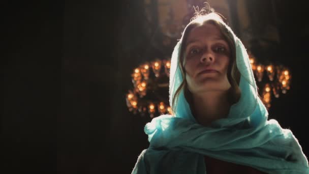 Jonge duizendjarige vrouw in roze jurk en blauwe hoofddoek staat in de kerk, tempel en bidt, kijkt naar de camera met een serieuze uitdrukking. Langzame beweging. — Stockvideo
