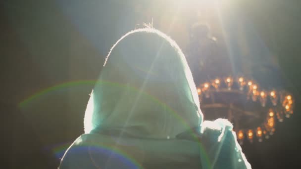 분홍색 옷을 입고 푸른 머리 스카프를 두른 젊은 천년기 여성이 교회, 사원, 기도에 등을 대고 카메라 앞에 서 있다. 느린 동작. — 비디오