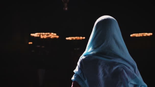 Молода тисячолітня жінка в рожевій сукні і синій хустці стоїть з нею спиною до камери в церкві, храмі і молитвах. Повільний рух . — стокове відео