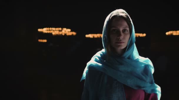 Jeune femme millénaire en robe rose et foulard bleu se tient à l'église, temple et prie, regarde la caméra avec une expression sérieuse. Mouvement lent. — Video