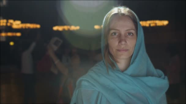 Jeune femme millénaire en robe rose et foulard bleu se tient à l'église, temple et prie, regarde la caméra avec une expression sérieuse. Mouvement lent. — Video
