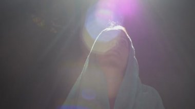 Pembe elbiseli ve mavi başörtüsü takmış genç bir kadın kilise, tapınak ve dua ediyor ve kameraya ciddi bir ifadeyle bakıyor. Yavaş çekim.