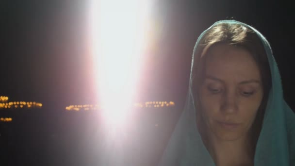 Young millennial woman in pink dress and blue headscarf stands in church, temple and prays, looks at the camera with a serious expression. Slow motion. — Stock Video