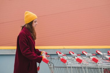 Burgonya paltolu ve sarı şapkalı genç bir kadın süpermarketin otoparkında yürüyor ve tramvaya biniyor..