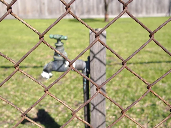 Paslı demiri çitin arkasında musluk suyu — Stok fotoğraf