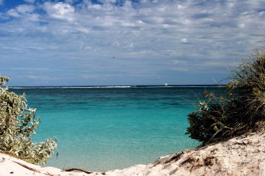 Pristine turquois waters through gap in the dunes