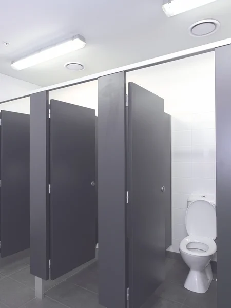Fila de cubículos sanitários em um banheiro industrial intocado — Fotografia de Stock