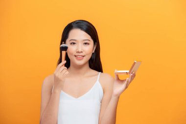 Kapalı Asyalı kadın sarı arka plan üzerine makyaj fırçası uygula .