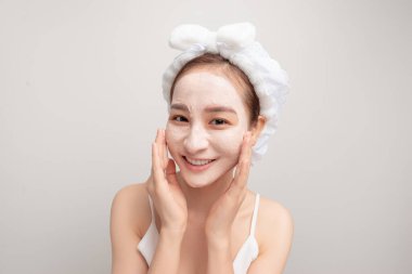 Tatlı bir genç kız spa tedavisinden zevk alıyor, yüzüne kilden bir maske takıyor, gülümsüyor.