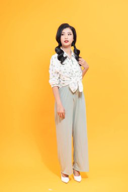 Uzun boylu, çekici, ince bir kız. Sarı arka planda izole edilmiş bir şekilde eğleniyor.