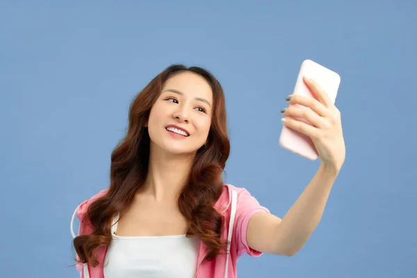 与情人手握智能手机 用蓝色背景隔离的前视镜拍摄自拍的冷静快乐女孩的肖像 — 图库照片