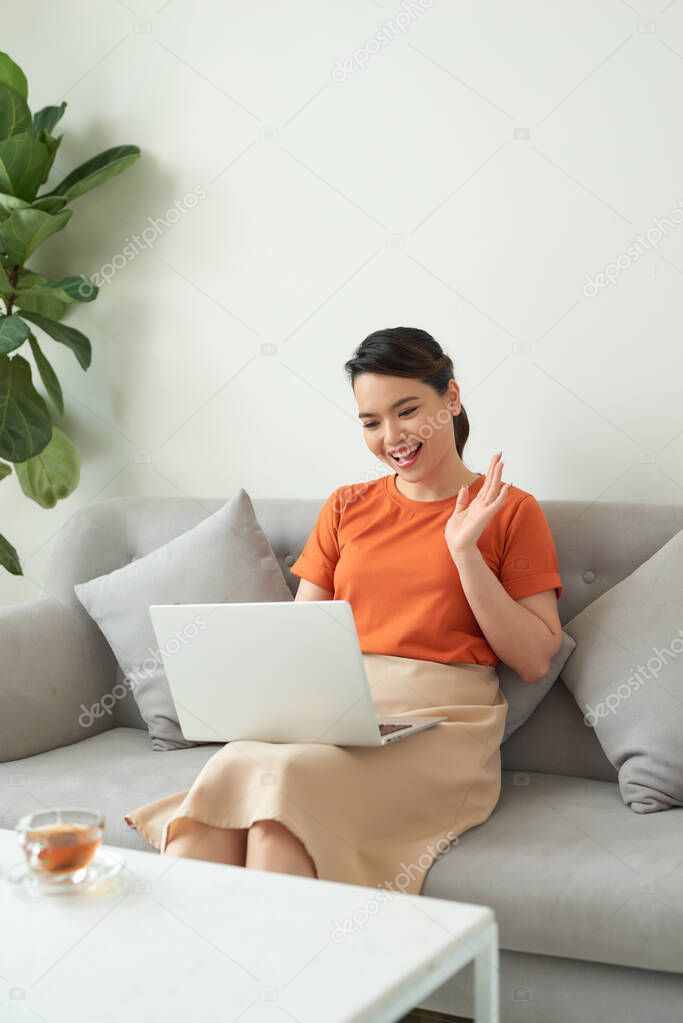 Smiling asian woman waving hand, using laptop, looking at screen. Online video chatting or online studying
