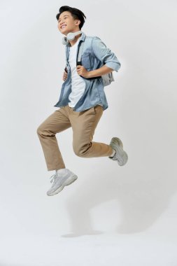 Kulaklıklı tam boy portre okullu adam müzik dinlerken beyaz ışıkta izole edilmiş.