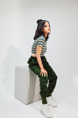 Örgü ören Asyalı kadın beyaz arka planda sandalyede oturuyor.