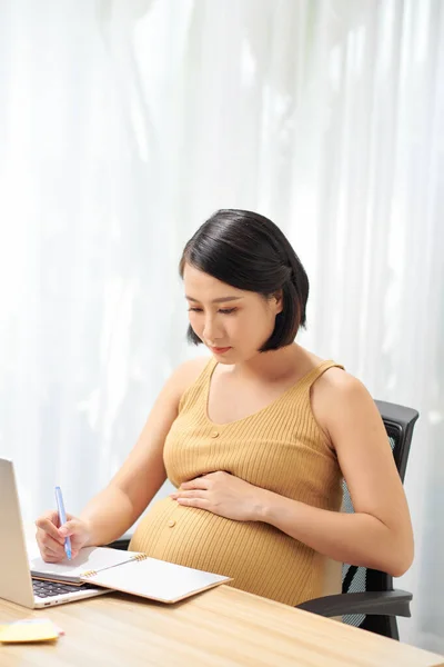 Schwangere Freiberuflerin Berührt Bauch Neben Laptop Schreibt Tagebuch Auf Tisch — Stockfoto