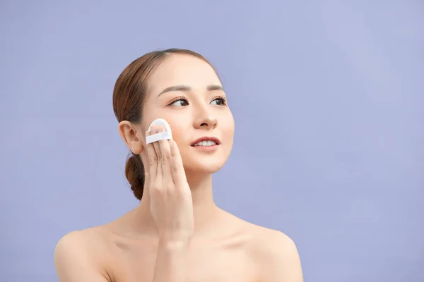 Beautiful woman applying dry powder using cosmetic cushion on her facial skin. Photo of attractive girl with perfect makeup on beige background. Beauty concept