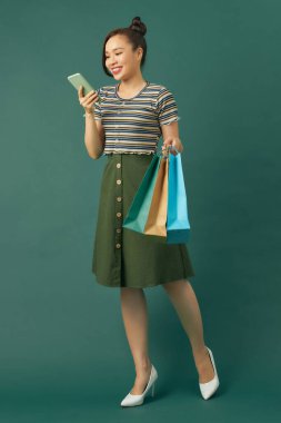 Mutlu Asyalı kadın gülümseyen yüzlü arka plan alışveriş merkezleri olan akıllı telefonu kullanıyor.