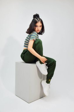 Moda kıyafetleri içinde şık bir kadın, arka planda bir sandalyede oturuyor.