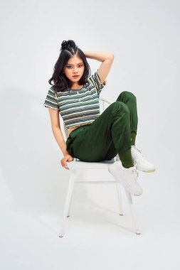 Tek kelimeyle muhteşem. Güzel genç bir kadın, beyaz arka planda otururken gülümseyerek poz veriyor ve uzaklara bakıyor.