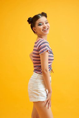 Parlak makyajlı ve sarı arka planda gülümseyen yaramaz Asyalı kadın.