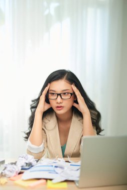 Başı ağrıyan yetişkin bir kadın ofiste dizüstü bilgisayarda çalışıyor.