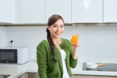 Çekici kadın mutfakta dikilirken elinde bir bardak portakal suyu tutuyor.