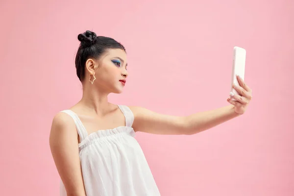一个漂亮的年轻女子用粉色背景的手机自拍的肖像 — 图库照片