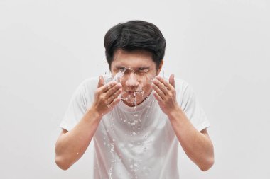 Yakışıklı adam bulaşık yıkıyor, su sıçrıyor, beyaz arka planda.