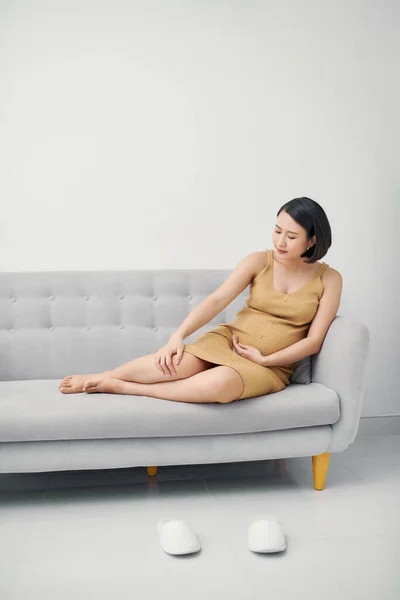 Wanita Asia Hamil Muda Yang Duduk Sofa Mengalami Nyeri Kaki — Stok Foto