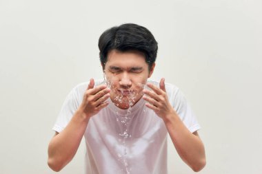 Yakışıklı adam yıkanıyor, su sıçrıyor, beyaz bir arka planda.