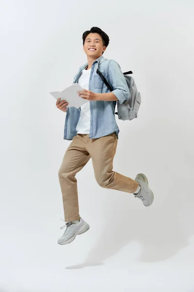 Счастливый Молодой Азиатский Студент Прыгает Воздух Рюкзаком Держа Книгу Белом — стоковое фото
